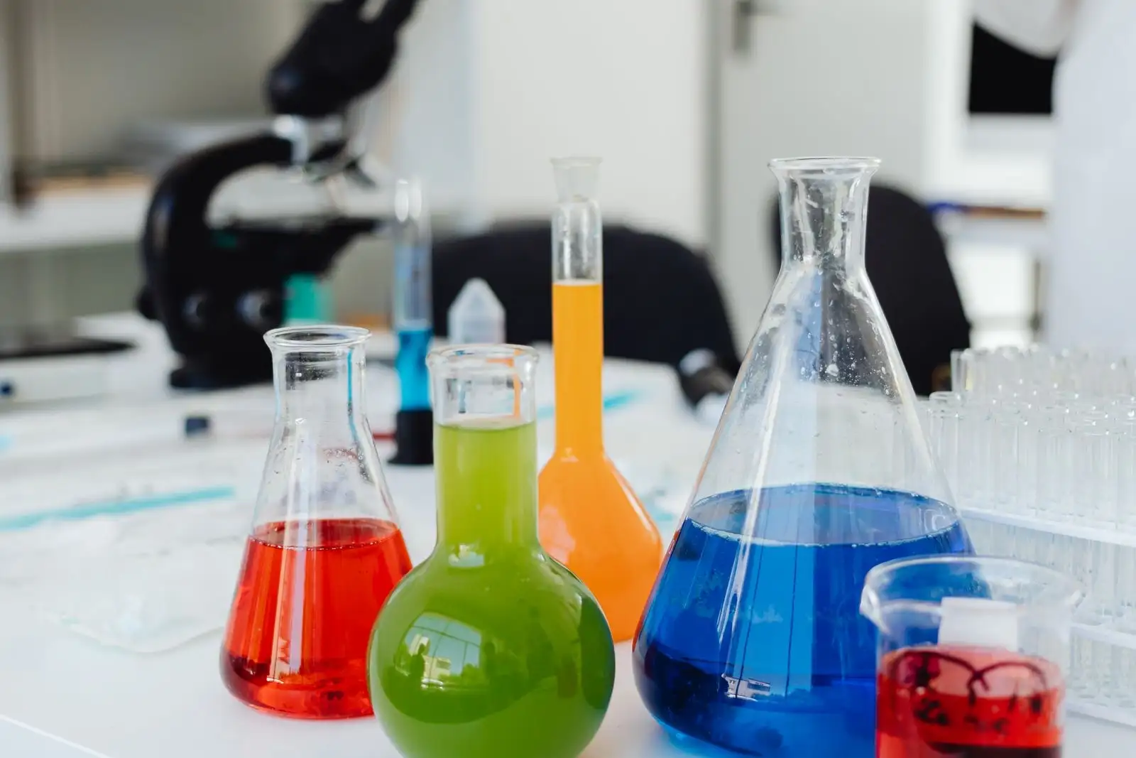 Material de vidrio de laboratorio sobre una mesa, matraces con líquidos de colores delante de un microscopio