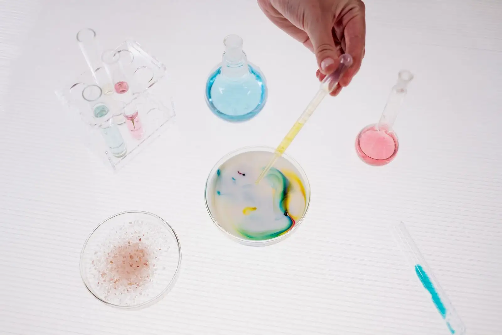 Pipeta que deja caer un líquido en una placa de Petri llena de una emulsión blanca, entre matraces y tubos de laboratorio