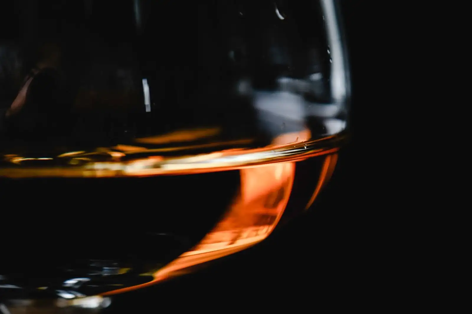 Copa de coñac en primer plano, un fondo de licor ámbar iluminado sobre fondo negro