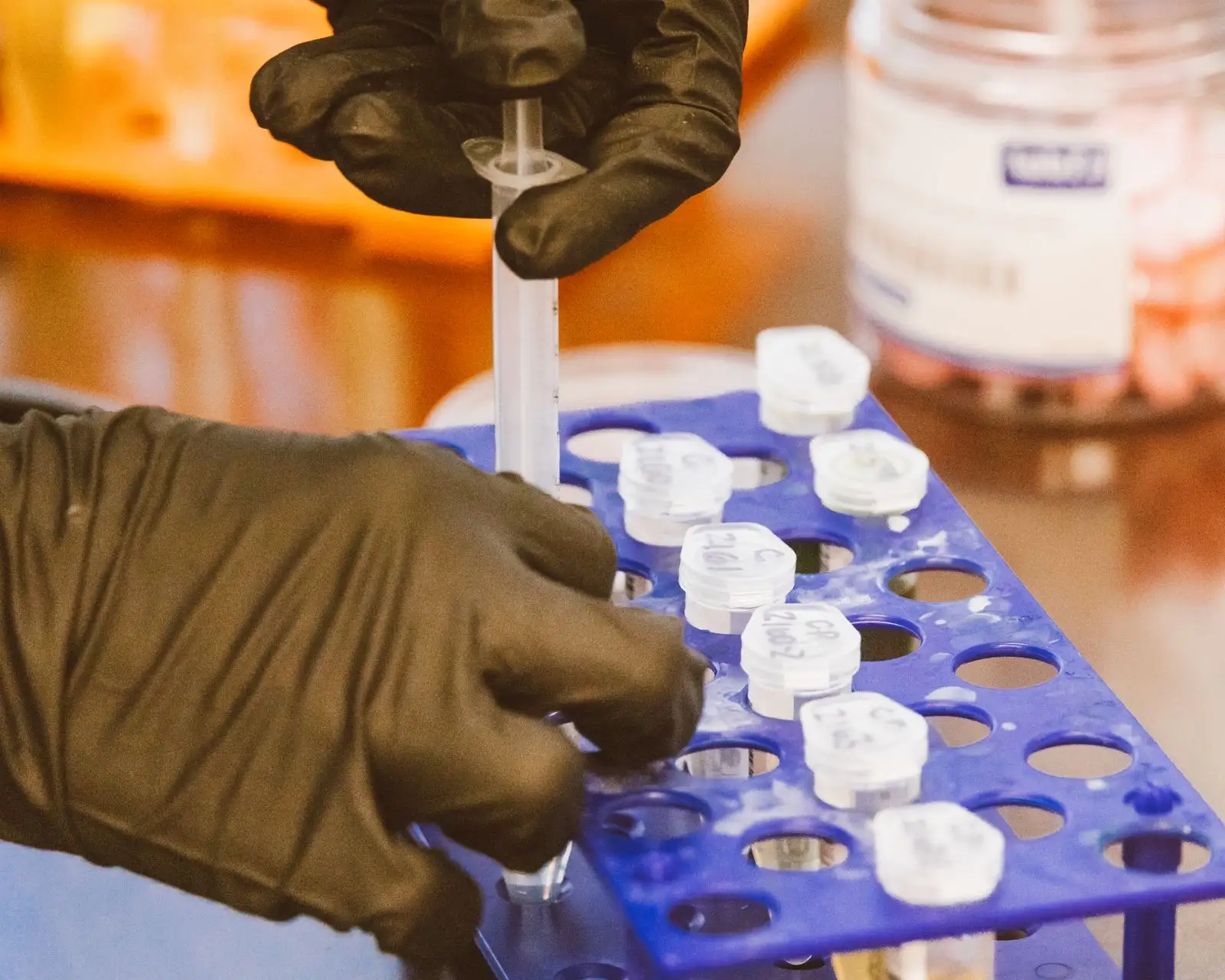 Manos con guantes colocando muestras en una gradilla de laboratorio, paso de preparación antes de un análisis cromatográfico