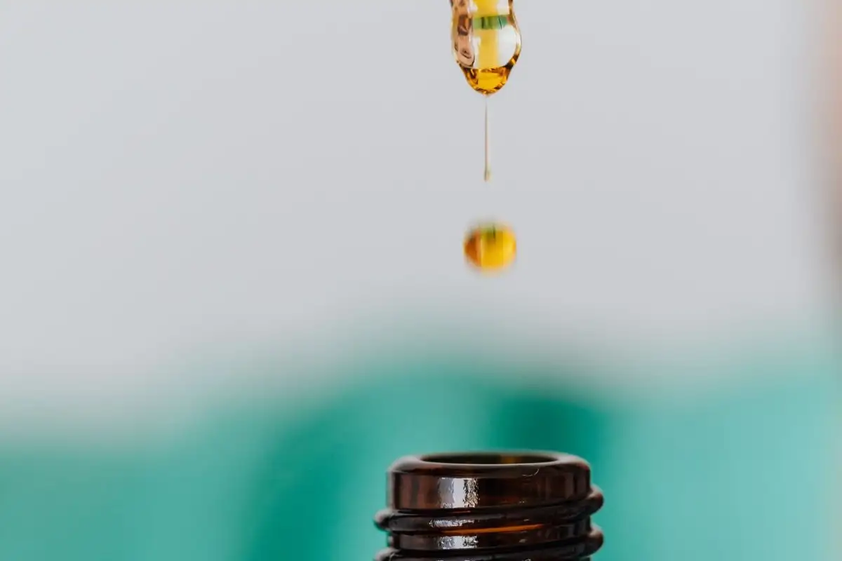 Una gota de aceite ámbar cae de una pipeta sobre un frasco de vidrio marrón