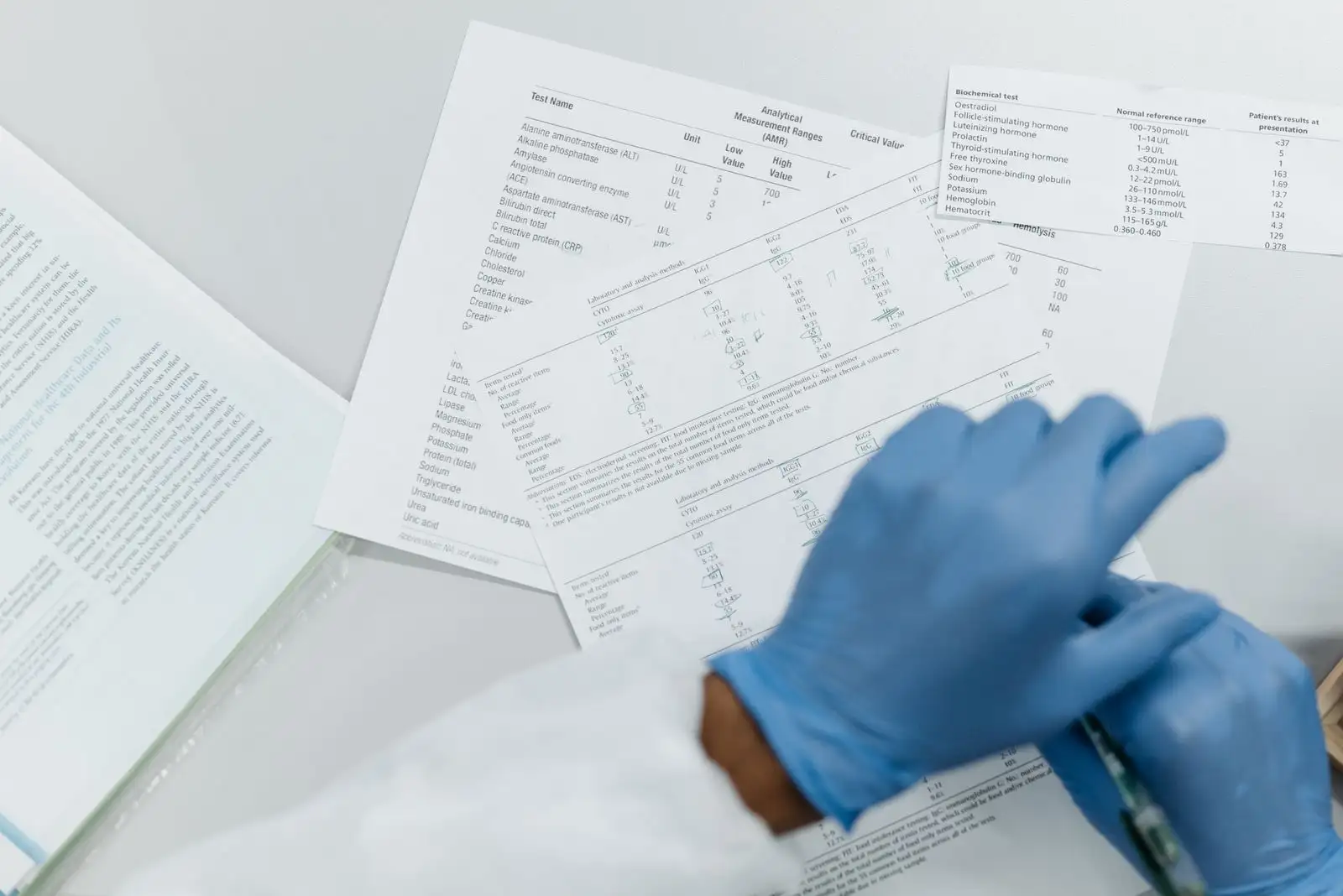 Manos con guantes revisando resultados de análisis de laboratorio impresos, tablas de valores sobre una mesa blanca