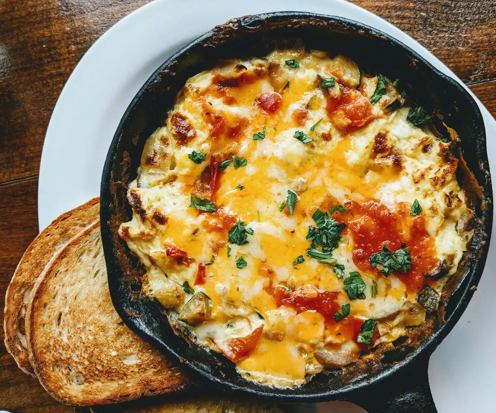 Tortilla gratinada con tomate y perejil en una sartén pequeña de hierro fundido, servida con dos rebanadas de pan tostado