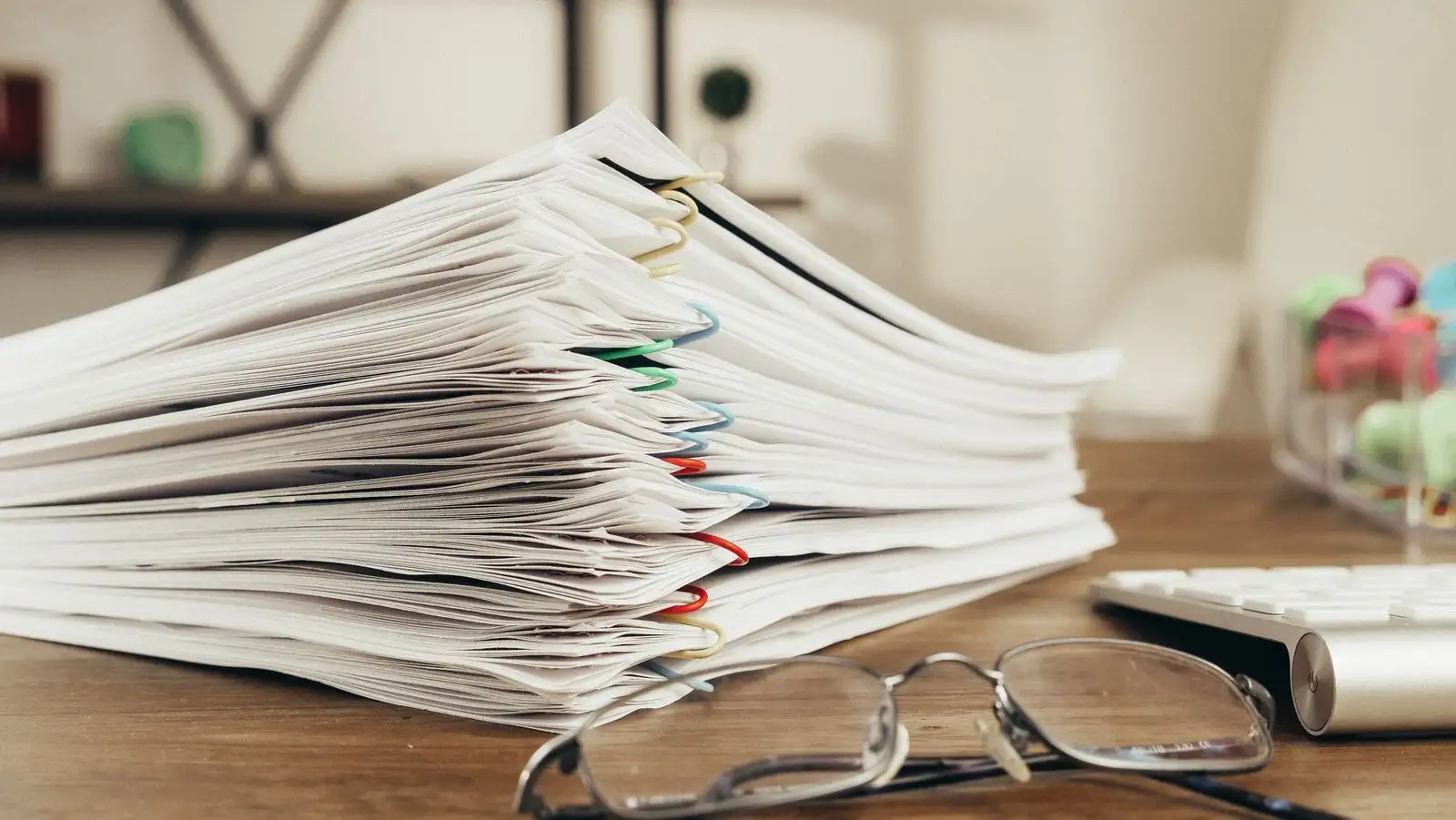 Pila de documentos grapados sobre un escritorio, junto a unas gafas