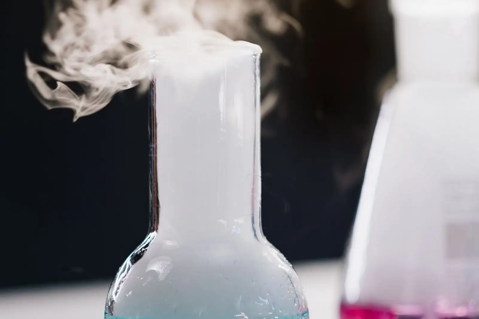 Matraz de laboratorio del que sale un vapor blanco, sobre fondo oscuro