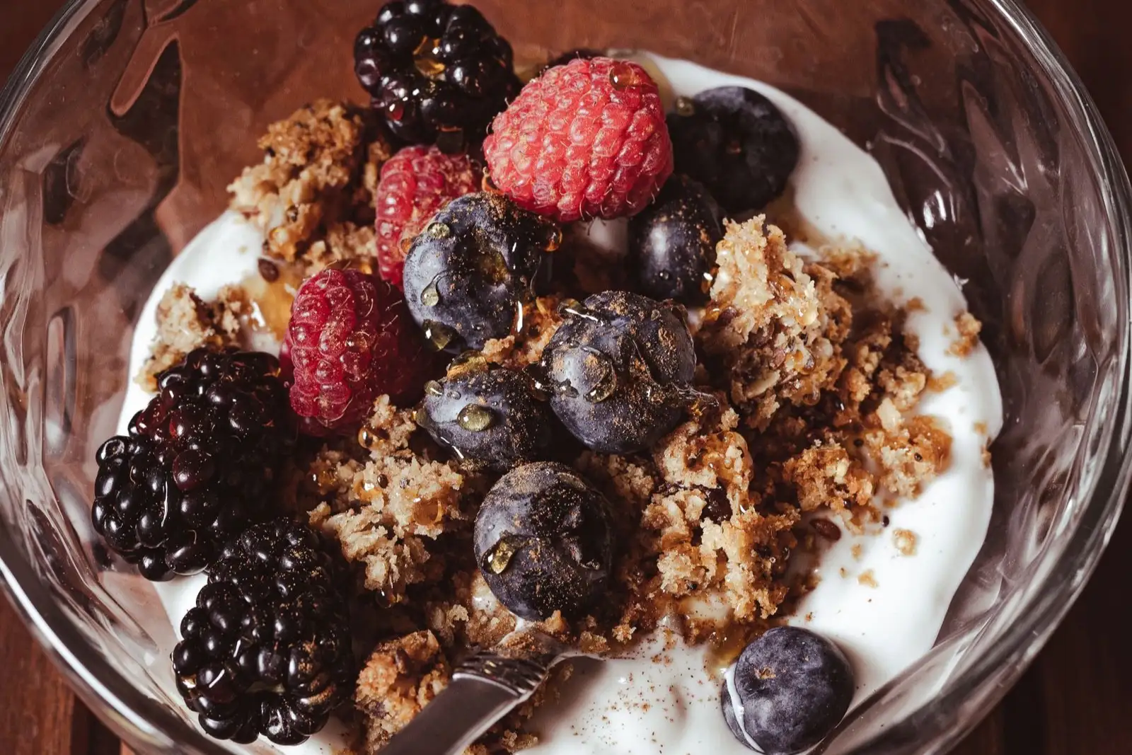 Cuenco de yogur espeso con granola, moras, frambuesas y arándanos, con una cuchara dentro