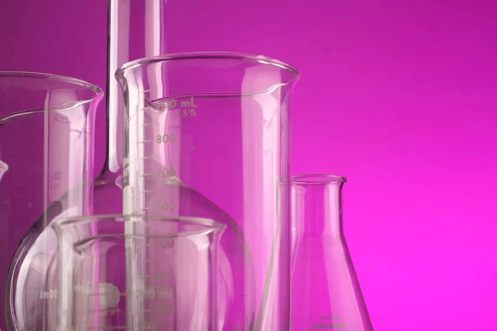 Material de vidrio de laboratorio graduado, matraces y vasos vacíos sobre fondo magenta