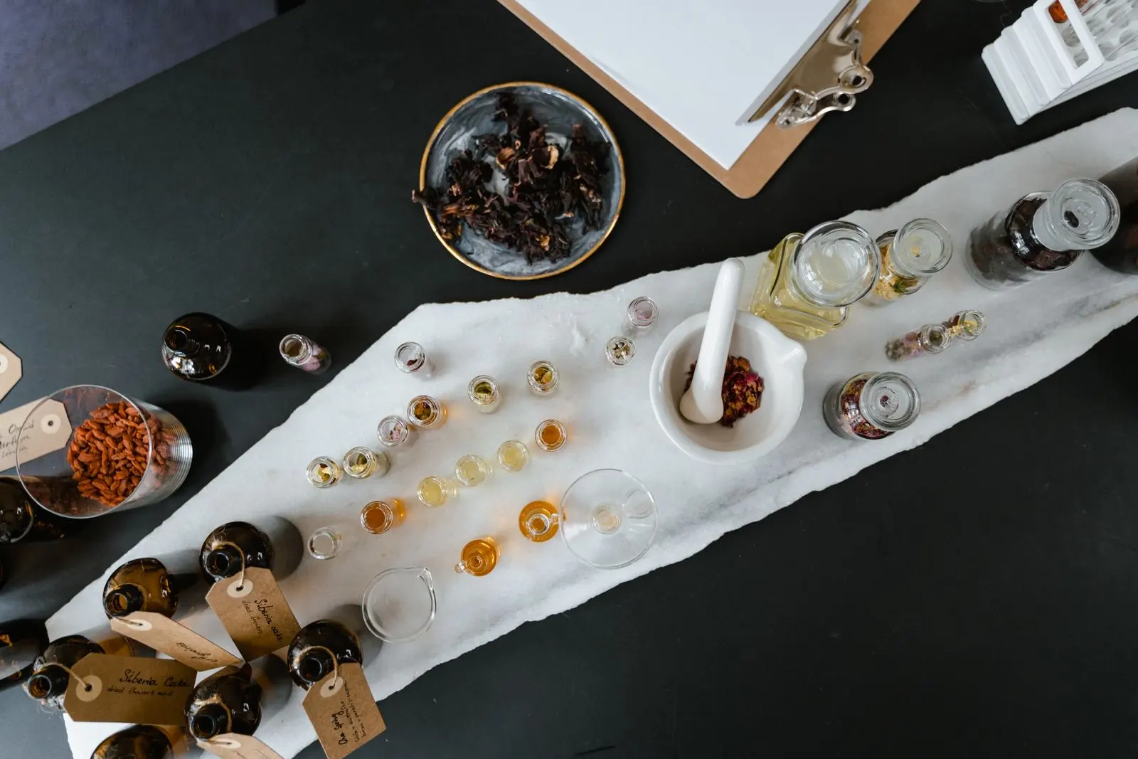 Frascos de aceite de vidrio ámbar y transparente, pipetas e ingredientes vegetales sobre una mesa, vistos desde arriba