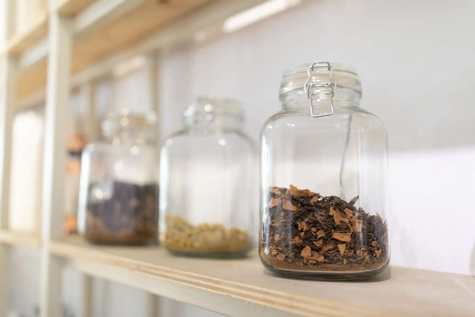 Tarros de cristal llenos de plantas secas alineados en una estantería de madera