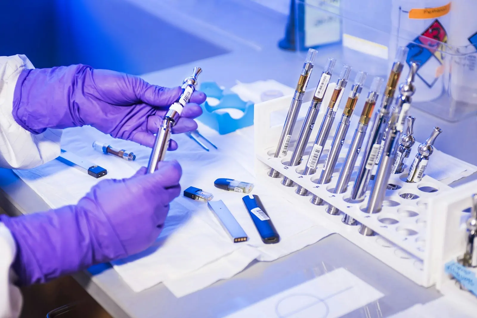 Manos enguantadas examinando cigarrillos electrónicos en un laboratorio de análisis, donde se identifican los cannabinoides sintéticos