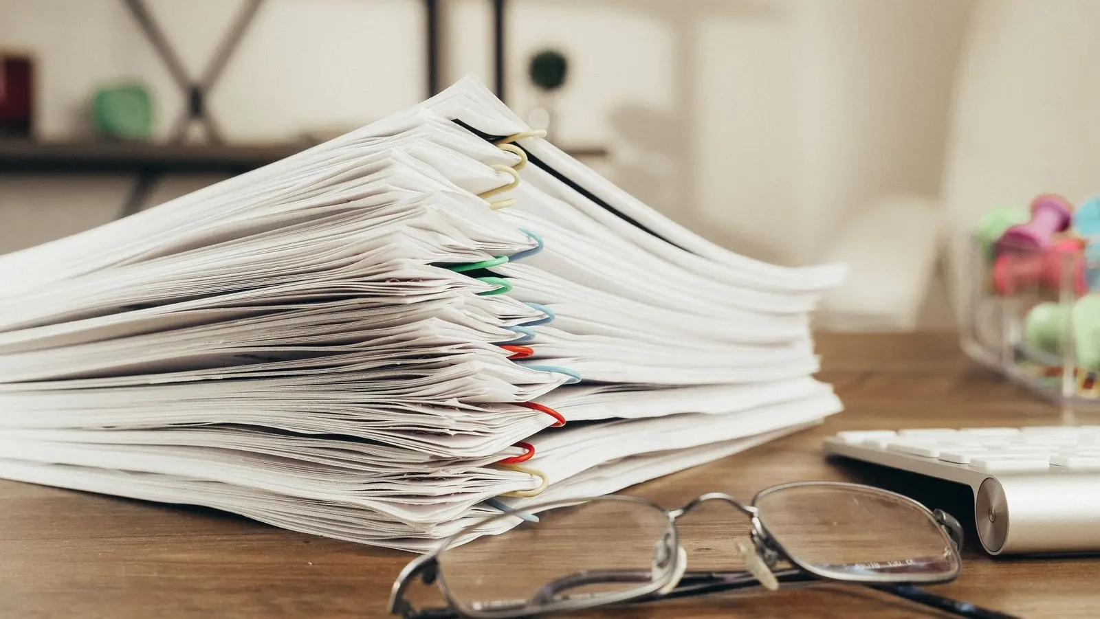 Pila de documentos grapados sobre un escritorio, junto a unas gafas