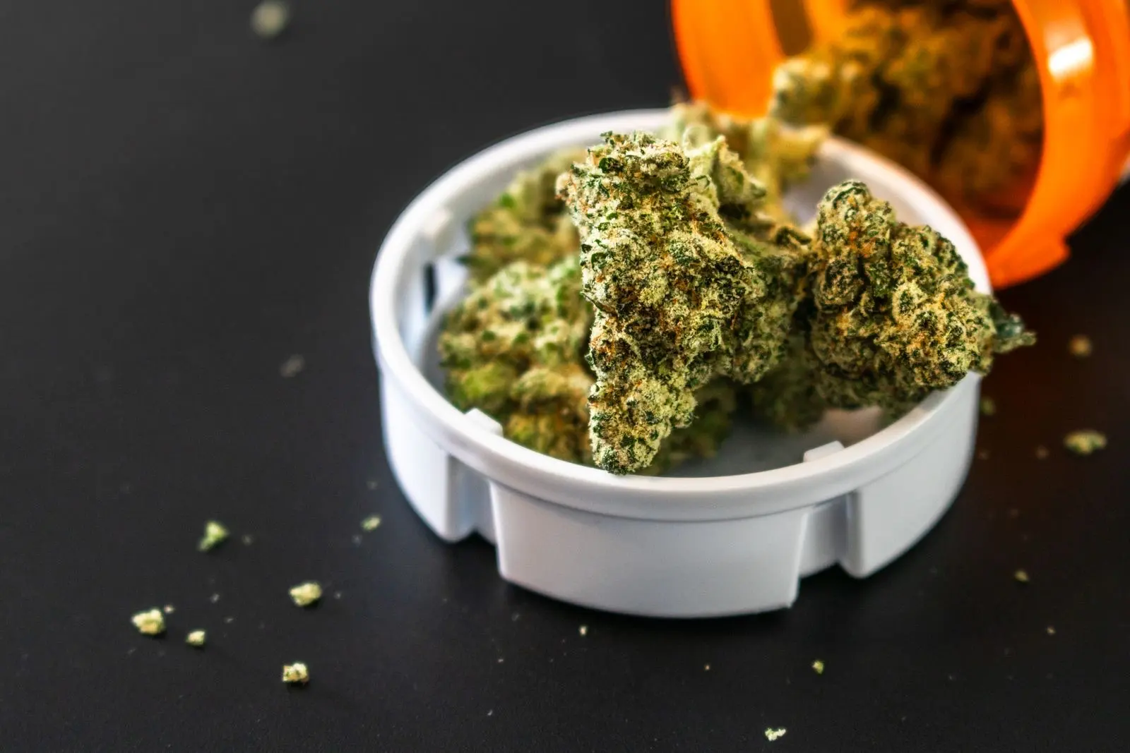 Cogollos de cannabis secos en la tapa de un bote naranja de farmacia volcado