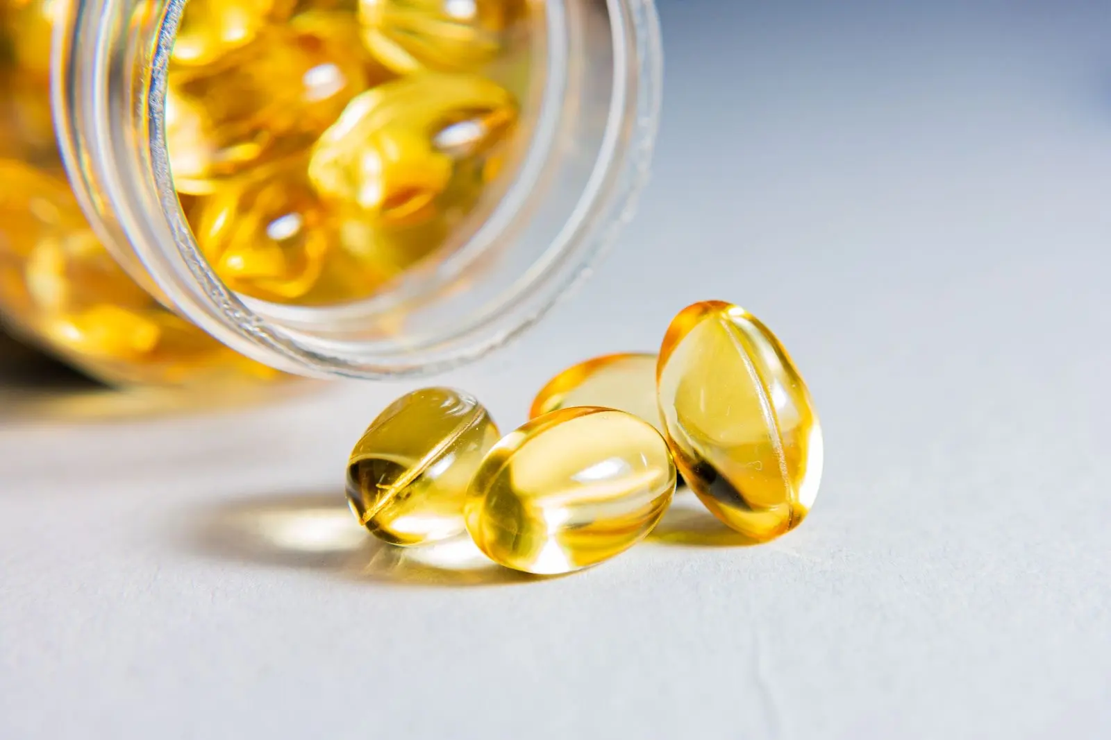 Cápsulas blandas transparentes llenas de aceite, saliendo de un frasco de vidrio
