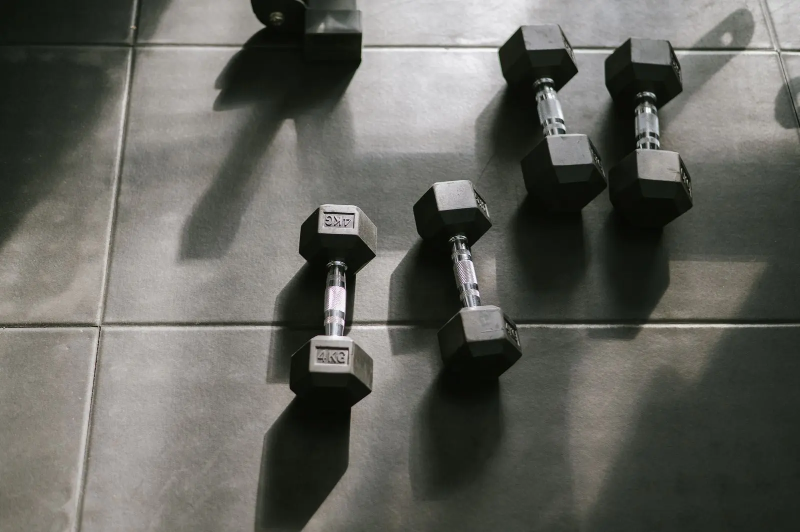 Mancuernas hexagonales de 4 kg en el suelo de un gimnasio, con luz rasante