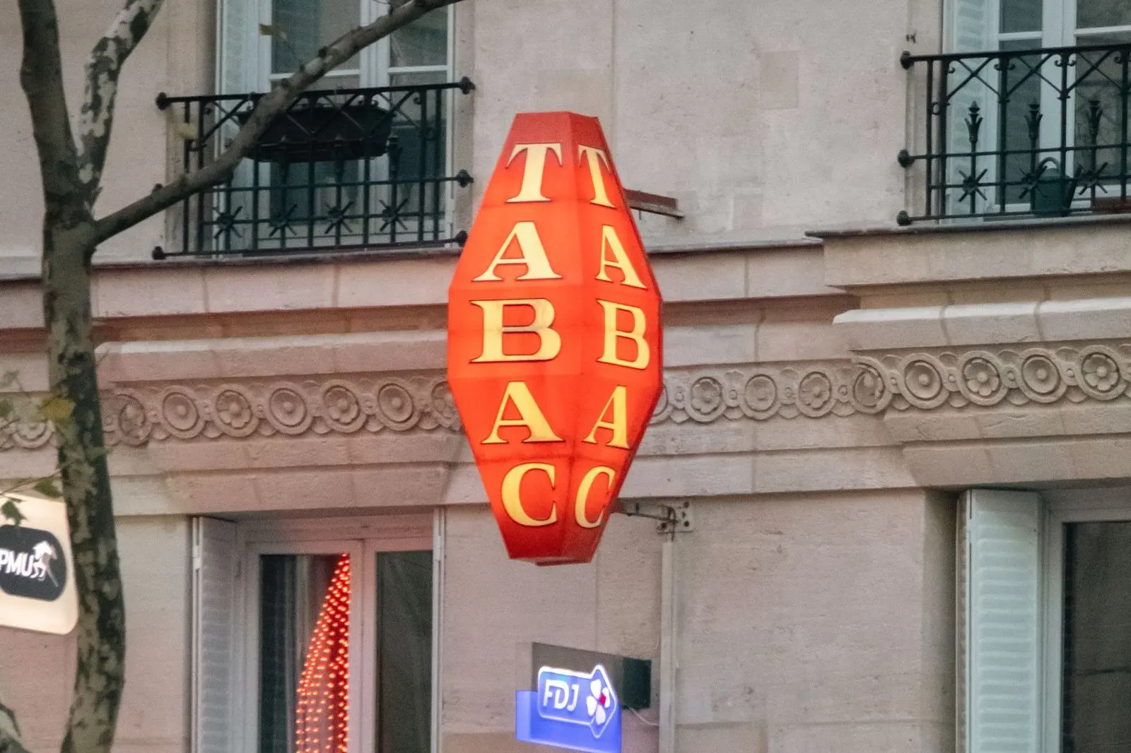 Letrero rojo en forma de rombo con la palabra «Tabac» en la fachada de un edificio de París