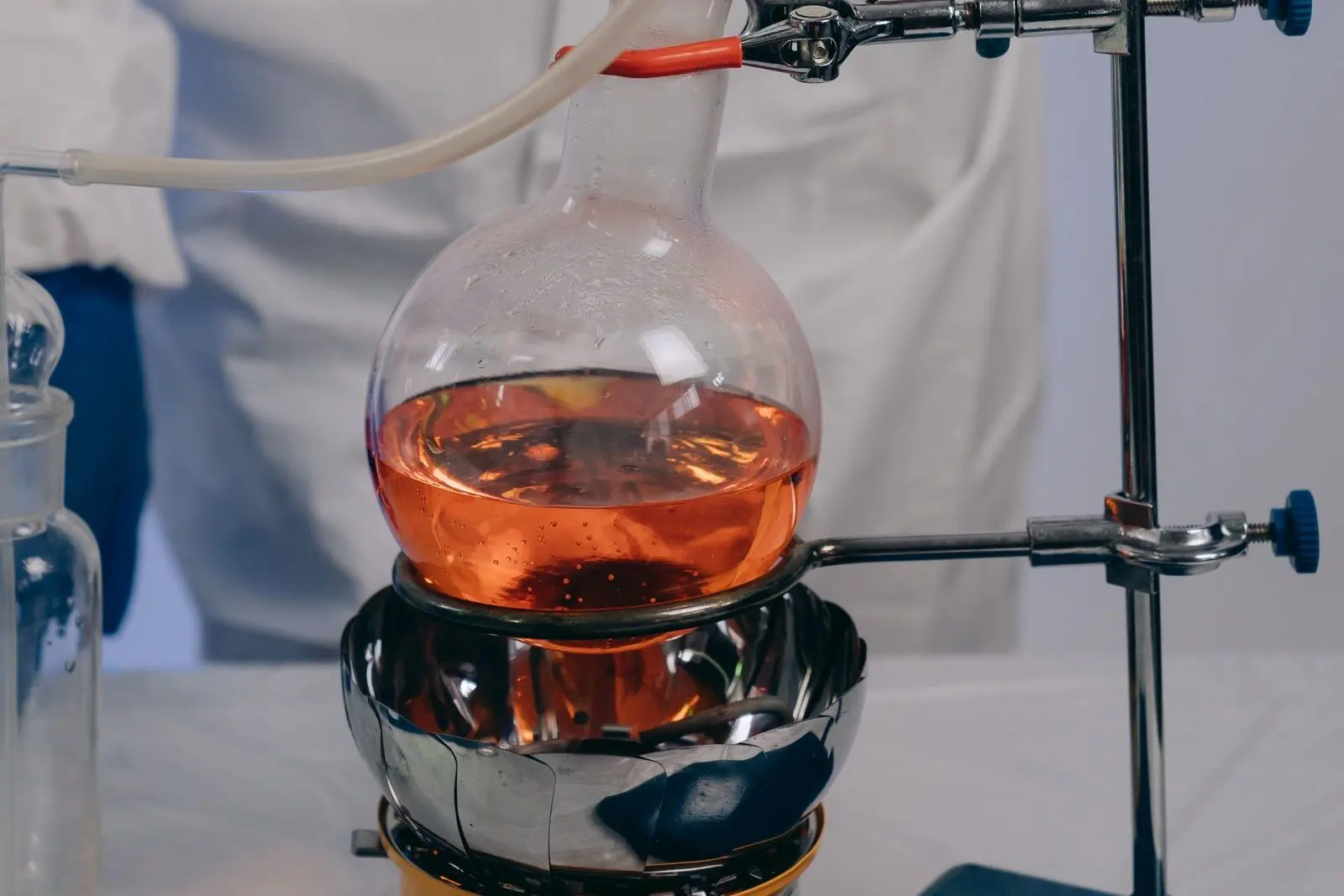 Matraz de laboratorio con un líquido anaranjado, sobre una manta calefactora y sujeto por una pinza